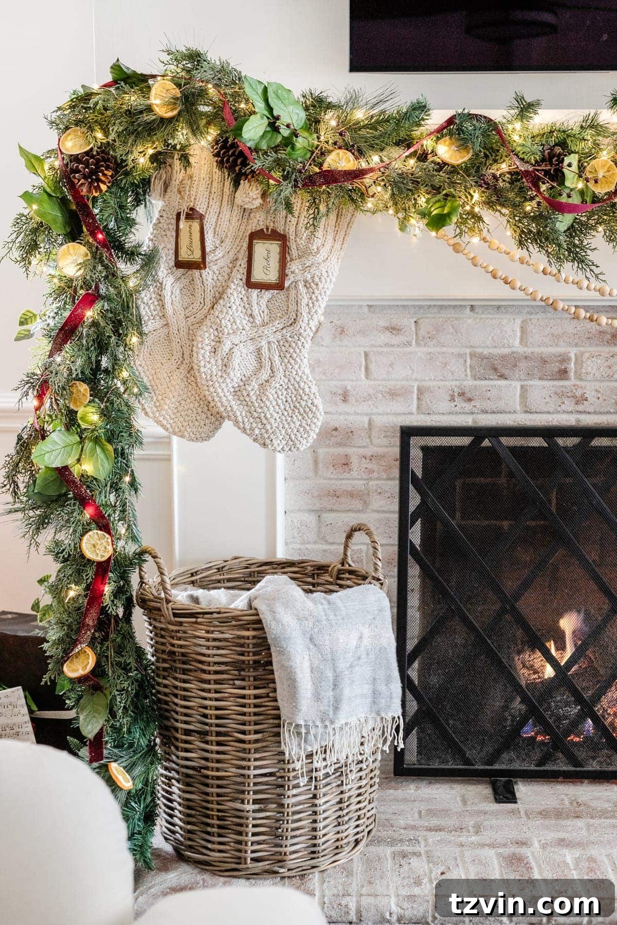 A beautifully embellished pine garland featuring pine cones, dried orange slices, layered leaves, fairy lights, and a festive red ribbon, showcasing a rich, traditional Christmas aesthetic.