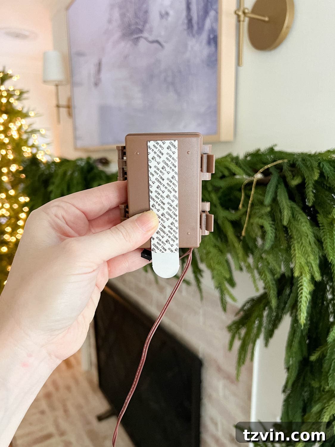 A close-up view of a fairy light battery pack discreetly attached to the underside of a mantel with a Command strip, highlighting a clever solution for hidden power.