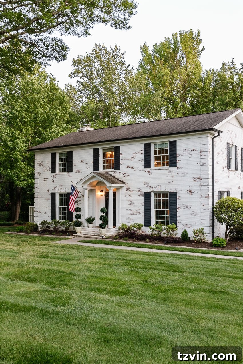 From Patchy to Pristine: Our Year-Long Lawn Makeover 3 A white limewashed brick colonial house now features a perfectly manicured, vibrant green lawn, enhancing its curb appeal significantly.