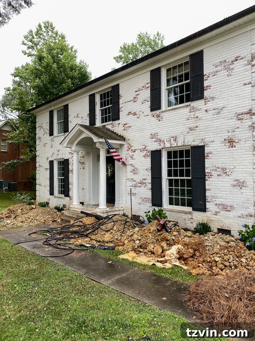 From Patchy to Pristine: Our Year-Long Lawn Makeover 5 A neglected front yard showing extensive foundation repairs in front of a brick house, with flower beds dug up and a sparse, damaged lawn.