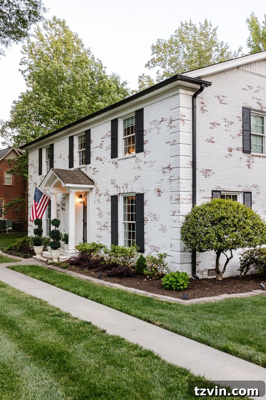 From Patchy to Pristine: Our Year-Long Lawn Makeover 6 A pristine white limewashed brick house with beautifully redone flower beds and a perfectly green, thriving lawn, showcasing a complete curb appeal facelift.