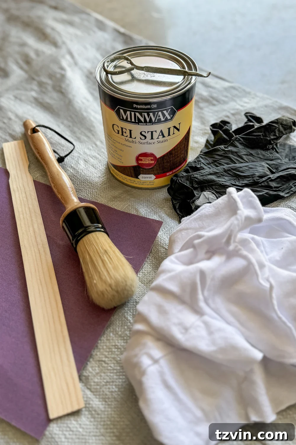 Renew Stained Furniture Without Sanding 4 Various gel stain furniture makeover supplies laid out, including Minwax gel stain, cleaners, sandpaper, rags, and brushes.