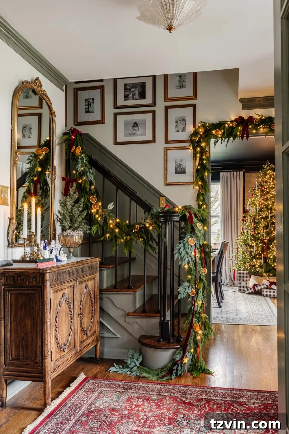 Beautifully decorated modern colonial Christmas entryway with festive garland on the staircase and elegant holiday decor.