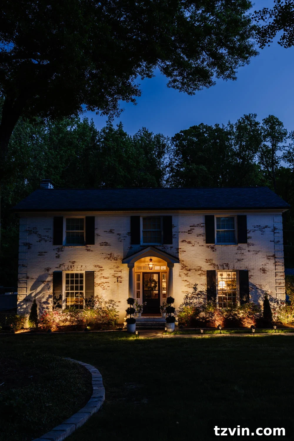Wow-Worthy DIY Front Yard Transformations 14 Evening view of a colonial house with solar spotlight landscape lights highlighting the front yard and home exterior