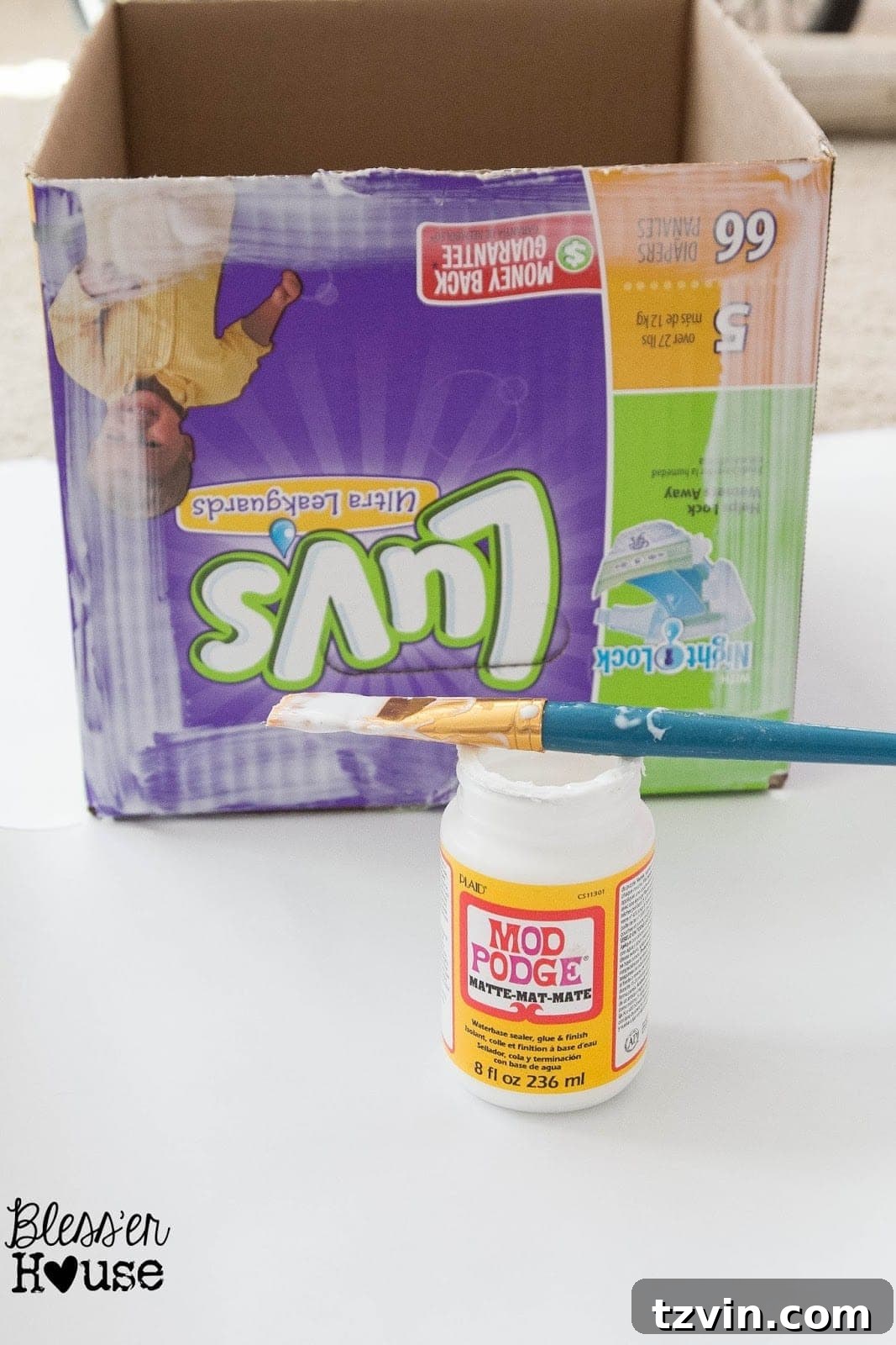 Applying Mod Podge to the side of a cardboard box before attaching the faux wood craft paper.
