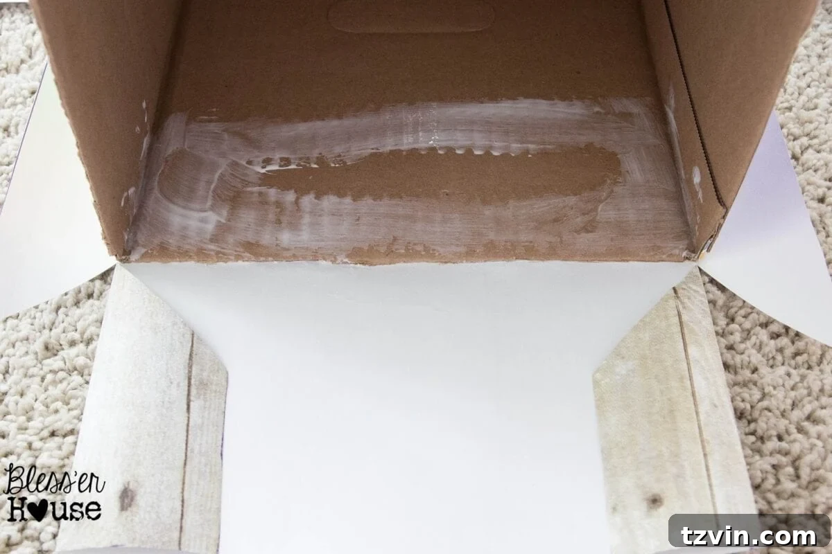 Mod Podge being brushed onto the inside top edge of the cardboard box for securing the paper.