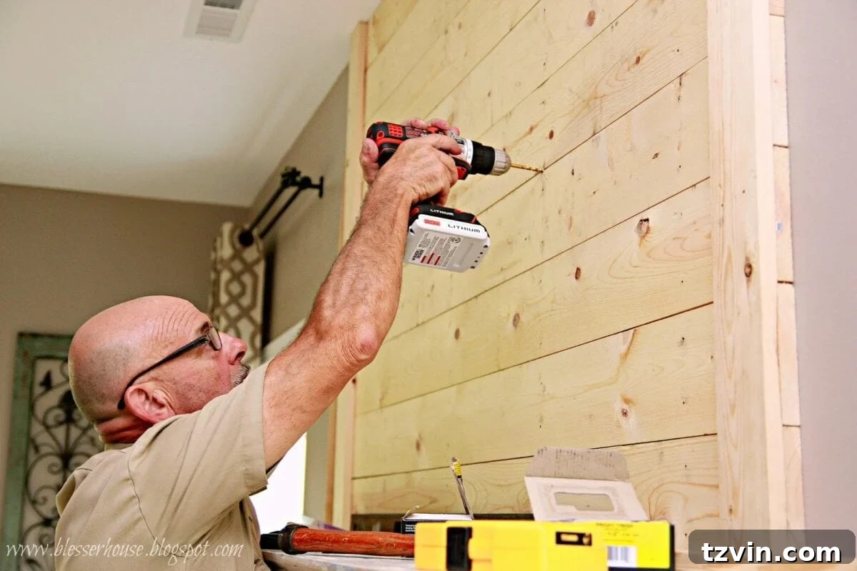 Drilling holes through the plank wall for secure TV mount installation directly into wall studs, ensuring stability.