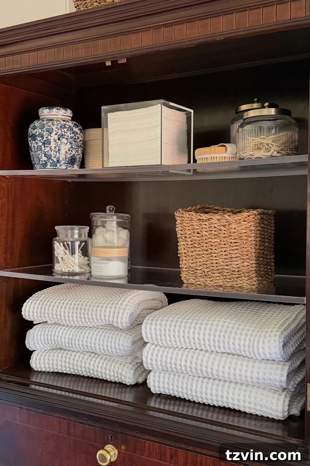 Repurposing a Secretary Desk: A DIY Makeup Vanity for Our Small Bathroom 6 Open top cabinet of a secretary desk vanity, neatly organized with folded waffle towels and apothecary jars containing cotton balls and Q-tips, in a modern vintage bathroom.